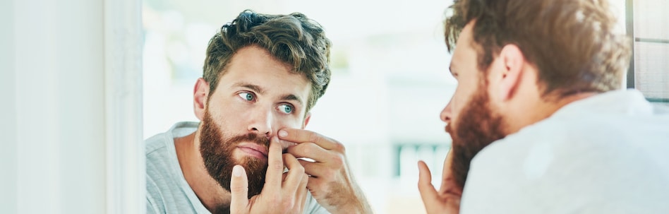 man popping a pimple in the mirror